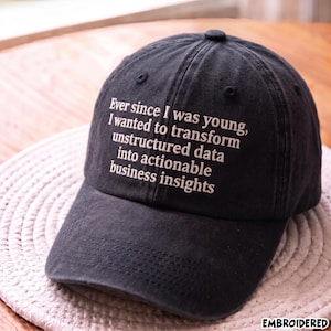 Könnte beinhalten: Eine schwarze Baseballkappe mit sechs Paneelen und einem gebogenen Schirm. Auf der Vorderseite befindet sich ein weißer Sticktext mit dem Inhalt: Ever since I was young, I wanted to transform unstructured data into actionable business insights.