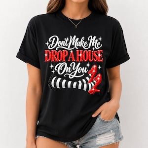 May include: A black t-shirt featuring the white text "Don't Make Me" and "On You" with the red glittery text "DROP A HOUSE" in the center. Below the text is a graphic of two legs wearing black and white striped stockings and red glittery shoes.