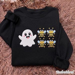 May include: A black long-sleeve crewneck sweatshirt featuring an embroidered white ghost with a smiling face and four small embroidered bees with yellow and black striped bodies and light blue wings arranged in a square pattern on the front.