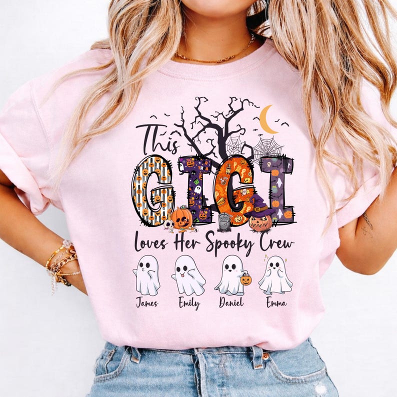 May include: A light pink t-shirt featuring a graphic with the text "This GIGI Loves Her Spooky Crew". The design includes large letters filled with Halloween patterns, a crescent moon, a tree, and four ghost illustrations labeled James, Emily, Daniel, and Emma.