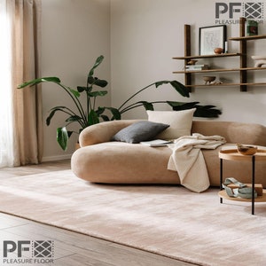 Puede incluir: Una alfombra rectangular grande de color beige claro con una textura suave y afelpada que cubre el suelo. La alfombra presenta un color sólido y uniforme con un pelo denso, proporcionando una base neutra para los muebles y la decoración.