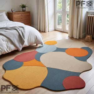 Puede incluir: Alfombra de área abstracta con un diseño geométrico colorido que presenta varios tonos de rojo, naranja, amarillo, azul y beige. La alfombra tiene una forma irregular y orgánica y una textura suave y mullida.