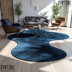 May include: A large, deep blue rug with an organic, flowing shape. The rug is the focal point of a modern living room, complemented by a grey sofa, armchairs, and a black coffee table. The room is bathed in natural light, creating a bright and airy atmosphere.