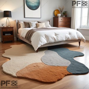 May include: A white bed with a brown headboard and a white duvet cover sits on a light wood floor. The bed is decorated with pillows in various shades of brown and beige. A large, abstract painting hangs on the wall behind the bed. A fluffy, multi-coloured rug with a unique, abstract design is placed under the bed. The rug features shades of beige, brown, grey, and teal.