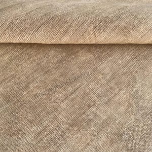 May include: Close-up of a beige woven rug with a textured surface. The rug has a rolled edge at the top, revealing the fabric's thickness and weave. The color is a neutral tone, suitable for various interior design styles.