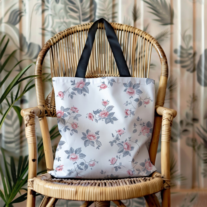 May include: A white tote bag with a floral pattern featuring pink and gray roses. The bag has black handles and is sitting on a wicker chair.