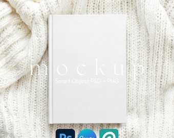 May include: A white book mockup with the word "mockup" in a light font. The book is on a white knitted blanket. Below the book are the logos for Photoshop, Canva, and Placeit.