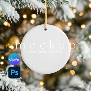 May include: A white, round Christmas ornament with a hole at the top, hanging from a gold string. The word "mockup" is printed on the ornament. The background is a blurred image of a Christmas tree with lights and snow.