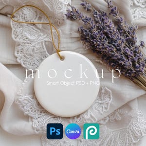 Op de afbeelding: Een witte, ronde keramische ornament met een gouden draad, met het woord "mockup". Een bos gedroogde lavendel en pictogrammen van ontwerpsoftware zijn ook zichtbaar. Het ornament ligt op witte kanten stof.