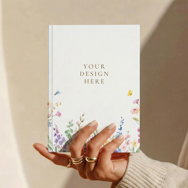May include: A white hardback notebook featuring a watercolour illustration of colourful wildflowers and a small yellow butterfly at the bottom. The centre of the cover displays the text YOUR DESIGN HERE in a simple, dark brown serif font.