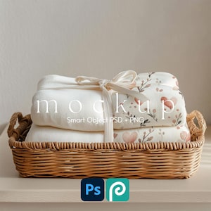 May include: A woven wicker basket holds folded white blankets tied with a cream ribbon. One blanket has a floral heart pattern. The word "mockup" is printed on the blankets. The basket sits on a light-colored surface.