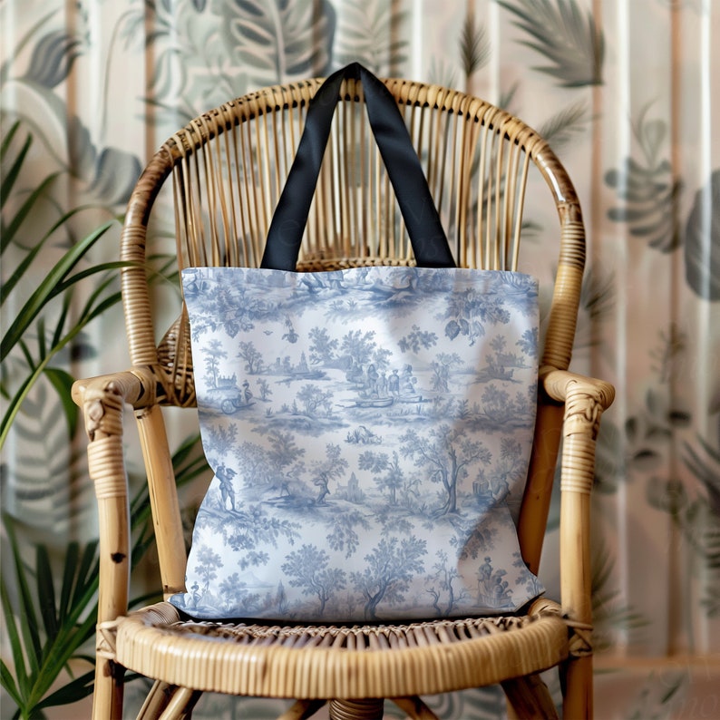 May include: A blue and white toile patterned tote bag with black handles. The bag is sitting on a wicker chair.