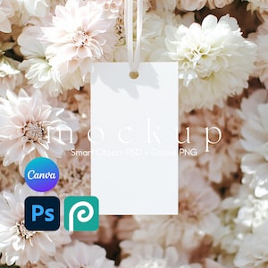 Puede incluir: Una etiqueta de regalo blanca en blanco con un agujero perforado en la parte superior, colgando de una cinta blanca. La etiqueta está rodeada de un ramo de flores blancas y crema.