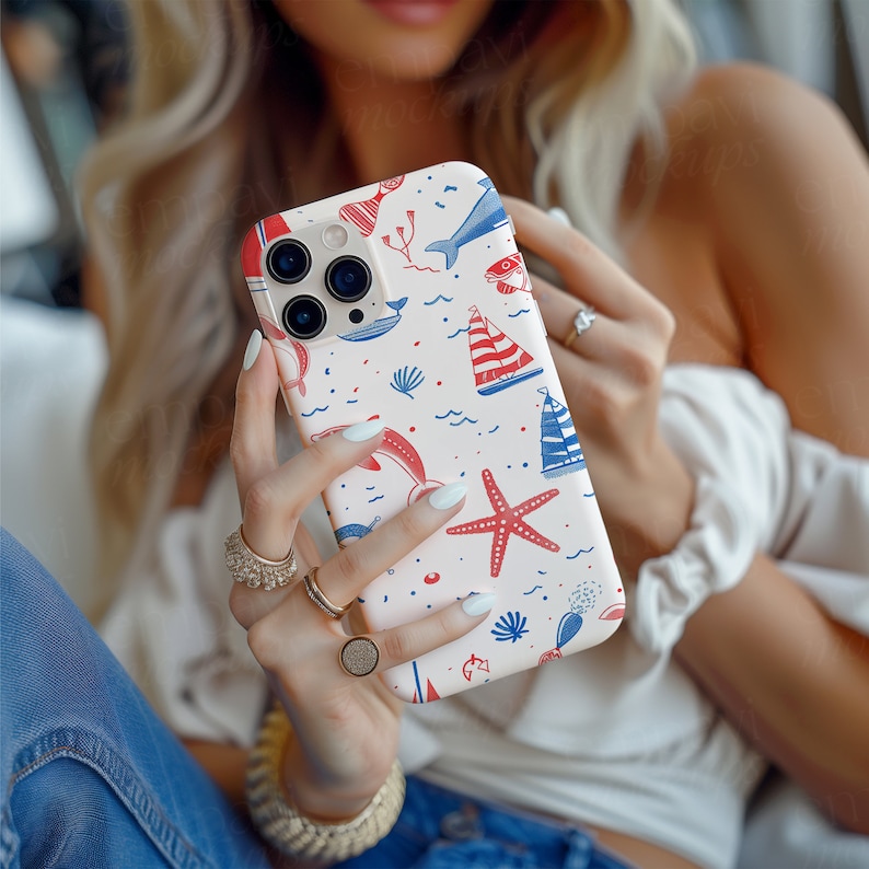 Op de afbeelding: Een telefoonhoesje met een nautisch thema. De hoes heeft een witte achtergrond met rode en blauwe illustraties van zeilboten, dolfijnen, zeesterren en andere zee-elementen. De hoes wordt door een persoon vastgehouden.