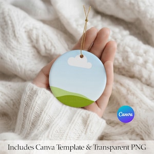 May include: A round ceramic ornament featuring a light blue sky, a single white cloud, and green rolling hills. The ornament is suspended by a thin gold string and includes a Canva template and transparent PNG file for customization.