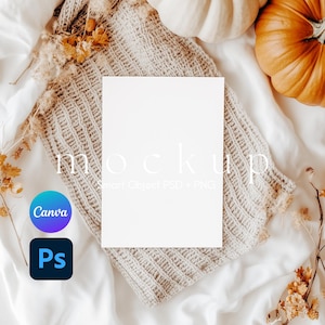 May include: A vertical white rectangular paper mockup centered on a beige knitted fabric. The image features the text mockup Smart Object PSD + PNG, a blue and purple Canva logo, and a black Photoshop logo. Orange pumpkins and dried flowers surround it.