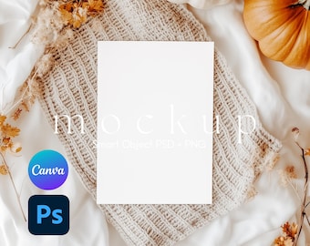 May include: A vertical white rectangular paper mockup centered on a beige knitted fabric. The image features the text mockup Smart Object PSD + PNG, a blue and purple Canva logo, and a black Photoshop logo. Orange pumpkins and dried flowers surround it.