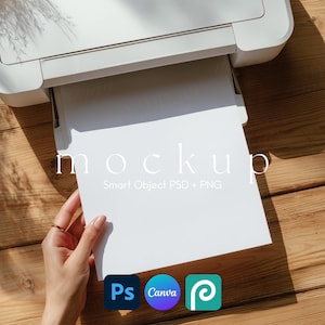 Puede incluir: Una impresora blanca con una maqueta de papel blanco en blanco. El papel lo sostiene una mano con un anillo dorado. El texto "mockup" está en el papel, junto con "Smart Object PSD + PNG". Los iconos de Photoshop, Canva y una herramienta de pluma están en la parte inferior derecha.