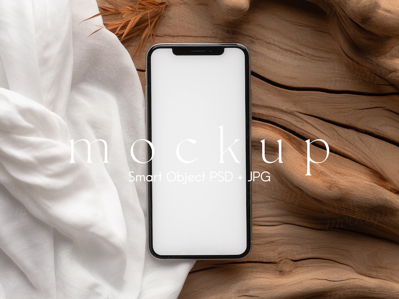 Blank black smartphone on natural wood with soft white fabric and dried leaves, creating a warm, organic setting for mobile design presentations