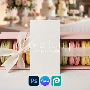 May include: A mockup image featuring a blank white card, a pink box of colorful macarons, and a cream-colored ribbon. The box is tied with a bow. The background includes wedding cakes and floral arrangements. The image also includes the text "mockup".