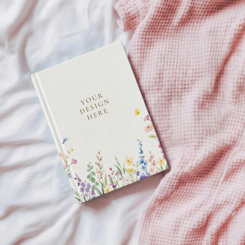 May include: A white hardback journal featuring a floral illustration along the bottom edge with various colourful wildflowers and greenery. The text "YOUR DESIGN HERE" is printed in dark lettering on the centre of the front cover.