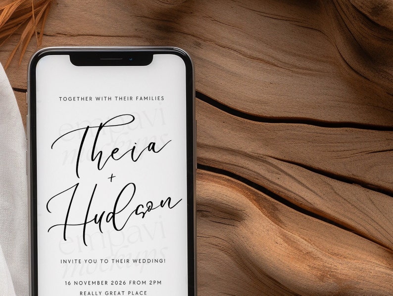 Blank black smartphone on natural wood with soft white fabric and dried leaves, creating a warm, organic setting for mobile design presentations
