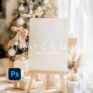 May include: A white blank canvas on an easel with a wooden frame. The canvas is set up in a room with a Christmas tree and presents. The text "mockup Smart Object PSD" is on the canvas.