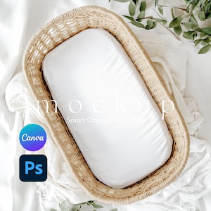 Puede incluir: Una sábana bajera blanca dentro de una cesta de mimbre tejida, perfecta para accesorios de fotografía de recién nacidos. La cesta está sobre un fondo de tela blanca con hojas verdes.