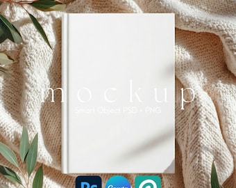 May include: A white book mockup with the word "mockup" in a light font. The book is on a cream-colored knitted blanket, with green leaves in the corners. The bottom of the image has the logos for Photoshop, Canva, and PicMonkey.