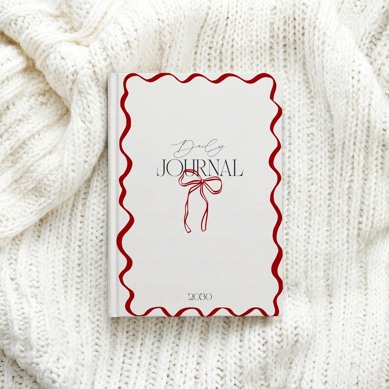 May include: A white journal with a red wavy border and the words "Daily Journal" in a script font. A red bow illustration is below the text, and the year "2030" is at the bottom. The journal is on a white knitted surface.