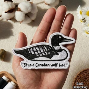 May include: Embroidered patch with a black and white loon design and the text "Stupid Canadian wolf bird." The patch has a white border and is suitable for clothing or accessories.