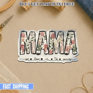 Pode incluir: Um patch branco com a palavra "MAMA" em letras contornadas a preto, preenchido com desenhos florais em rosa, pêssego e verde. O texto "we love u to pieces" está por baixo. O patch está numa superfície bege.