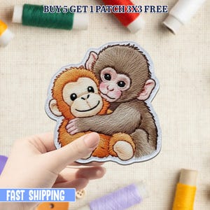 Peut inclure: Écusson brodé représentant deux singes de dessin animé qui s'embrassent. Un singe est brun, l'autre est orange. L'écusson est tenu par une main, avec des bobines de fil en arrière-plan. Le texte en haut indique "BUY 5 GET 1 PATCH 3X3 FREE".