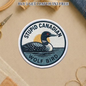 May include: Circular embroidered patch with a loon design, a yellow sun, and the words "STUPID CANADIAN WOLF BIRD". The patch has a white border and is set against a tan backdrop. The patch is a circular shape.