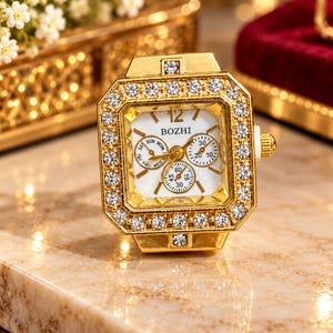 May include: A gold-toned square ring watch featuring a white face with the brand name BOZHI, three sub-dials, and a bezel encrusted with clear crystals. The watch face displays the number 12 at the top and includes a small crown on the side.