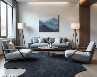 May include: A living room with a gray sofa, two gray armchairs, two floor lamps, a coffee table, and a gray rug. The rug has a unique, organic shape. A framed print of a mountain landscape hangs on the wall.