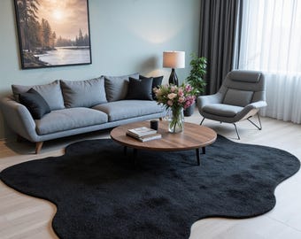 May include: A black shag rug with a unique cloud-like shape, placed in a living room setting with a gray sofa, a coffee table, and a gray armchair. The rug is in the center of the room, with the furniture arranged around it.