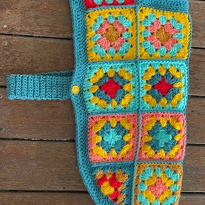 Pu&ograve; includere: Un giubbotto per cani in crochet blu turchese con una cinghia e una chiusura a bottone. Il giubbotto &egrave; realizzato con quadrati della nonna in tonalit&agrave; turchese, giallo, rosa e rosso.