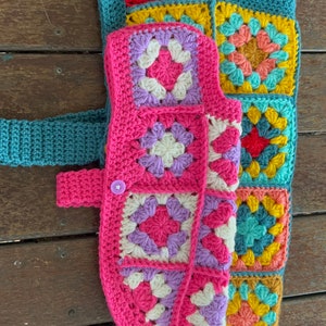 Pu&ograve; includere: Un giubbotto per cani all'uncinetto con un design a patchwork colorato. Il giubbotto &egrave; realizzato con quadrati della nonna in tonalit&agrave; di rosa, viola, blu, giallo e verde.