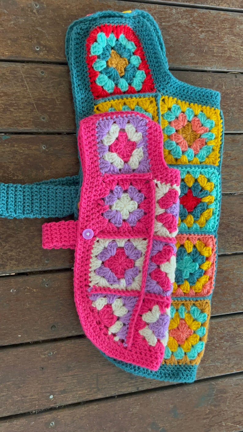 Pu&ograve; includere: Un giubbotto per cani all'uncinetto con un design a patchwork colorato. Il giubbotto &egrave; realizzato con quadrati della nonna in tonalit&agrave; di rosa, viola, blu, giallo e verde.