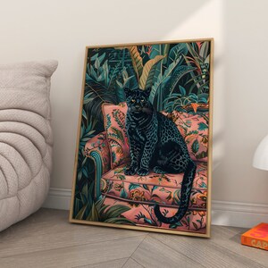 May include: A black panther sits on a pink floral patterned armchair in a lush green jungle setting. The panther is looking directly at the viewer. The artwork is framed in a gold frame.