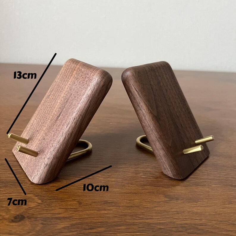 May include: Two wooden phone stands with brass accents. The stands are 13 cm tall, 10 cm wide, and 7 cm deep.