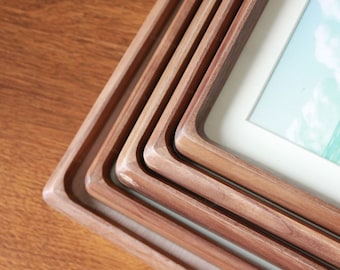 May include: A set of four wooden picture frames, nested together, with a light brown finish. The frames are square and have a simple, modern design.