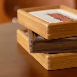 May include: Three wooden picture frames stacked. The top and bottom frames are light brown, the middle one is dark brown. The frames have a simple, rectangular design. The frames are likely for displaying artwork.