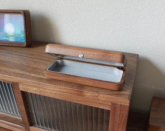 May include: A wooden box with a gray felt lining is open and sitting on a wooden surface. The box is made of dark wood and has a brass latch.