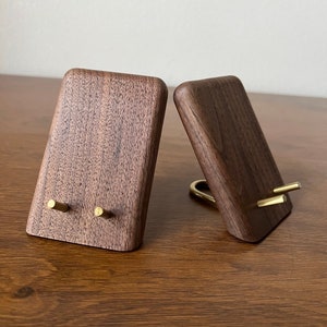 May include: Two wooden phone stands with brass accents. The stands are made of dark walnut wood and have a simple, modern design.