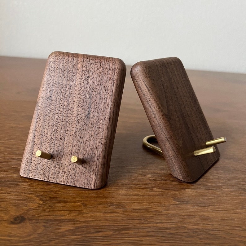 May include: Two wooden phone stands with brass accents. The stands are made of dark walnut wood and have a simple, modern design.