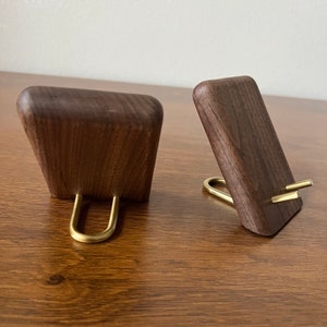 May include: Two wooden phone stands with brass accents. The stands are made of dark walnut wood and have a simple, modern design.