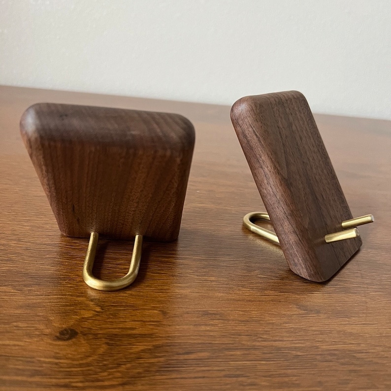 May include: Two wooden phone stands with brass accents. The stands are made of dark walnut wood and have a simple, modern design.