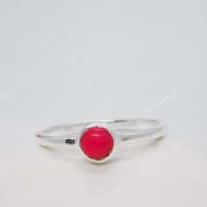 Peut inclure: Une bague en argent avec une pierre précieuse rouge vif sertie dans un sertissage à bélière.